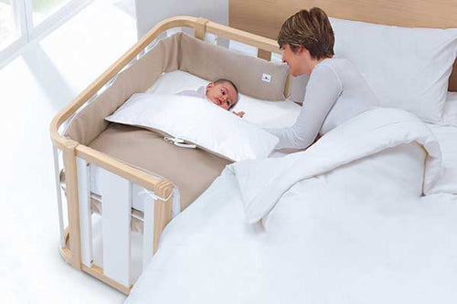 madre junto a bebé en una minicuna de madera blanca